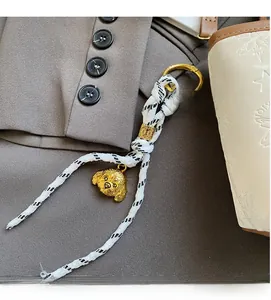 Detailed view of woven rope keychain with gold dog charm on a white fashion handbag