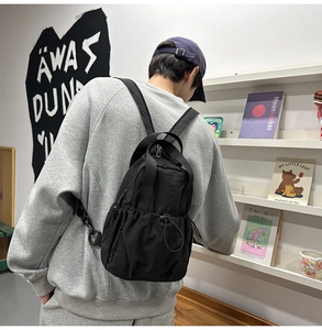 Detail of a lightweight black nylon backpack with drawstring pocket worn by a person