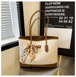 Detail of beige woven tote bag with brown leather handles and decorative silk scarf