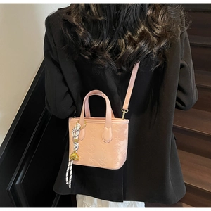 Detail of pink embossed bucket bag with gold bear charm and striped scarf on model