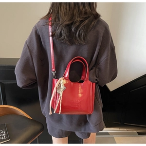 Dettaglio borsa a secchiello in vernice rossa con logo e ciondoli intrecciati su una modella