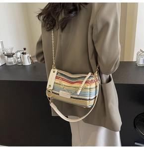Detail of colorful woven cylinder bag with gold chain strap shown in a cafe setting