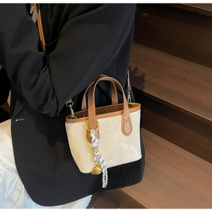 Detail of star-embossed beige bucket bag with brown trim and woven lanyard accent