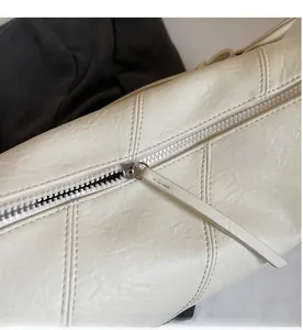 Detail of smooth metal zipper and textured pebble grain leather on creamy white tote bag