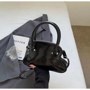 Detail of black patent leather shell bag with unique wavy base and silver hardware accents