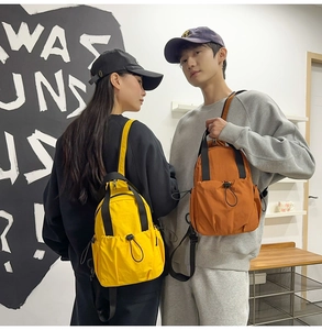 Detailed view of yellow and orange mini nylon backpacks worn by a model on a urban background