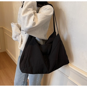 Lifestyle view of a large black nylon tote bag worn by a model in a minimalist hallway