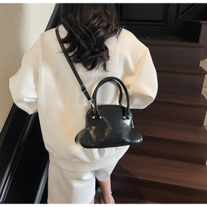 Detailed back view of a glossy black PU leather shell bag with silver hardware on stairs
