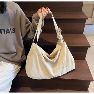 Detail of a large cream canvas hobo bag with a knotted strap worn by a model