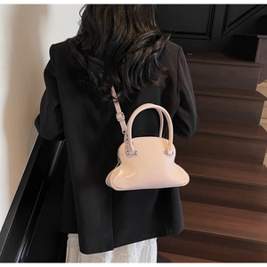 Rear view of model holding a pink glossy shell-shaped handbag on minimalist stairs