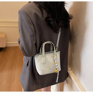 Detail of light grey bucket bag with star embossing, silk scarf and bear pendant