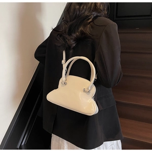 Detail of cream shell bag featuring glossy faux leather texture and silver hardware accents