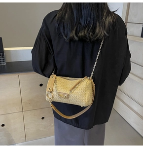Detail of woven straw cylinder bag with gold chain and brown leather shoulder strap