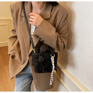 Detail of black embossed bucket bag with silk scarf and gold bear charm accessory