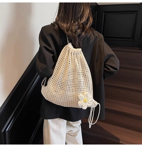 Détail d'un sac à dos en tricot ajouré blanc cassé avec une grande fleur 3D et cordon