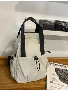 Lightweight cream nylon backpack with black straps and drawstring pockets on wood table
