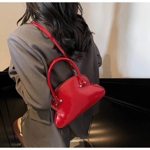 Detail showing bright red glossy shell bag on a model with silver hardware and ring handles