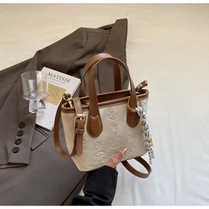 Detail view of cream embossed tote bag with brown straps and woven rope ornament