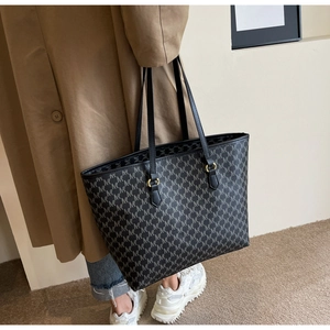 Detail of grey tote bag with monogram pattern and gold rings on slim black straps