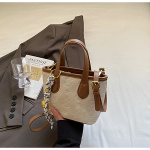 Detail view of cream bucket bag with star embossing and brown trim in a stylish setting