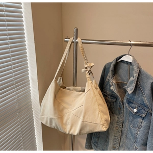 Detail of beige canvas tote bag with geometric stitching and decorative bow on shoulder strap