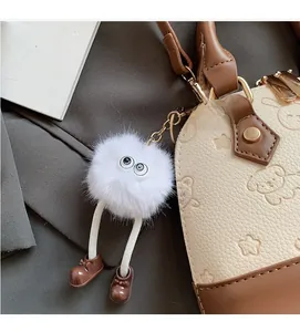 Close-up of a white plush monster charm with big eyes on a beige dog-embossed handbag