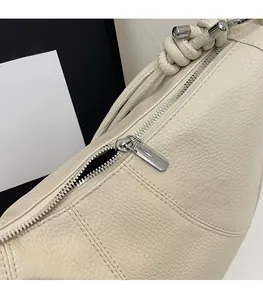 Detail of off-white lychee grain leather bag featuring a smooth metal zipper and rope knot strap
