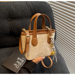 Detail of white leather bucket bag with star patterns, silk scarf and bear charm