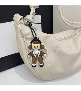 Detail of creamy white hobo bag with pebbled leather texture and cute doll charm accessory