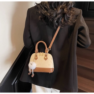 Close-up of beige shell bag featuring embossed bear patterns and a plush charm