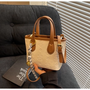 Detail of cream bucket bag featuring star embossing, brown trim, and woven bell charm