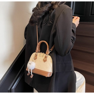 Close-up of beige shell bag with bear embossing, brown leather straps and plush charm
