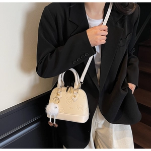 Detail of cream shell bag featuring embossed rabbit patterns and a plush charm