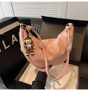 Detailed shot of pink crescent shoulder bag with lychee texture and cute cartoon pendant