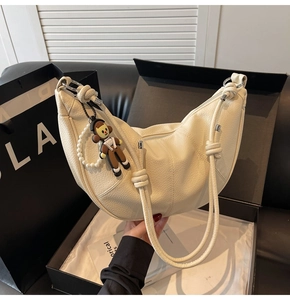 Detail of cream crescent bag featuring lychee grain leather and a cute doll pendant