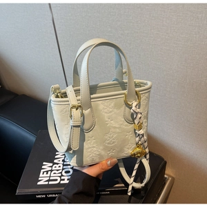 Detail of mint green bucket bag featuring star embossing and a gold bear charm accessory