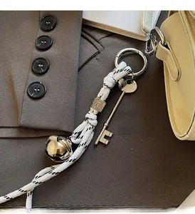 Detail of woven rope keychain with metal bell, key pendant, and decorative bead on bag