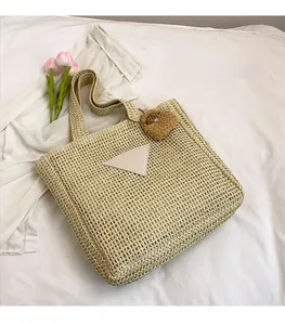 Détail d'un sac cabas en paille avec empiècement triangle en cuir et charm cœur en peluche