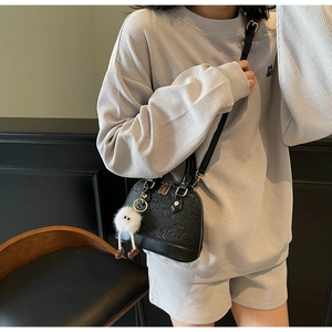 Detail of black shell bag with cartoon embossing and a white plush keychain accessory
