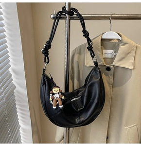 Detail of black crescent leather shoulder bag with textured finish and cute astronaut charm