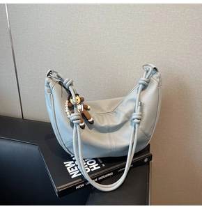 Detail of light blue lychee leather shoulder bag with a cute monkey charm and silver hardware