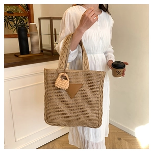 Détail du sac cabas en paille tissée avec écusson en cuir marron et breloque en maille