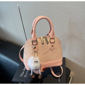 Detailed close-up of pink shell bag with cartoon prints and plush monster charm