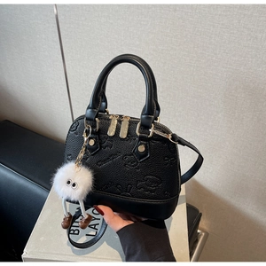 Detail of black shell bag with cartoon embossing and a white plush monster keychain