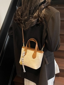 Elegant off-white embossed bucket bag with brown leather straps shown on a model