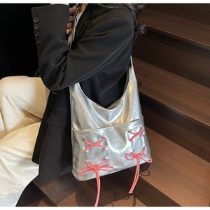 Close-up of metallic silver tote bag featuring decorative pink ribbon lace-up details