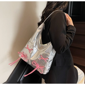 Silver metallic tote bag detail with pink bow ribbons worn by model on shoulder