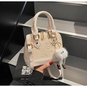 Close-up of cream shell bag with embossed cartoons and plush pendant on stairs