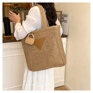Détail d'un grand sac cabas en paille avec accent cuir et mini breloque porté par un mannequin