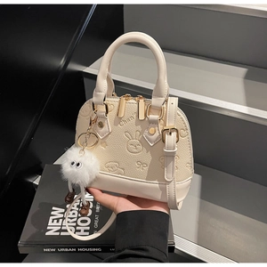 Detail of cream shell bag with embossed rabbit patterns and fluffy plush charm